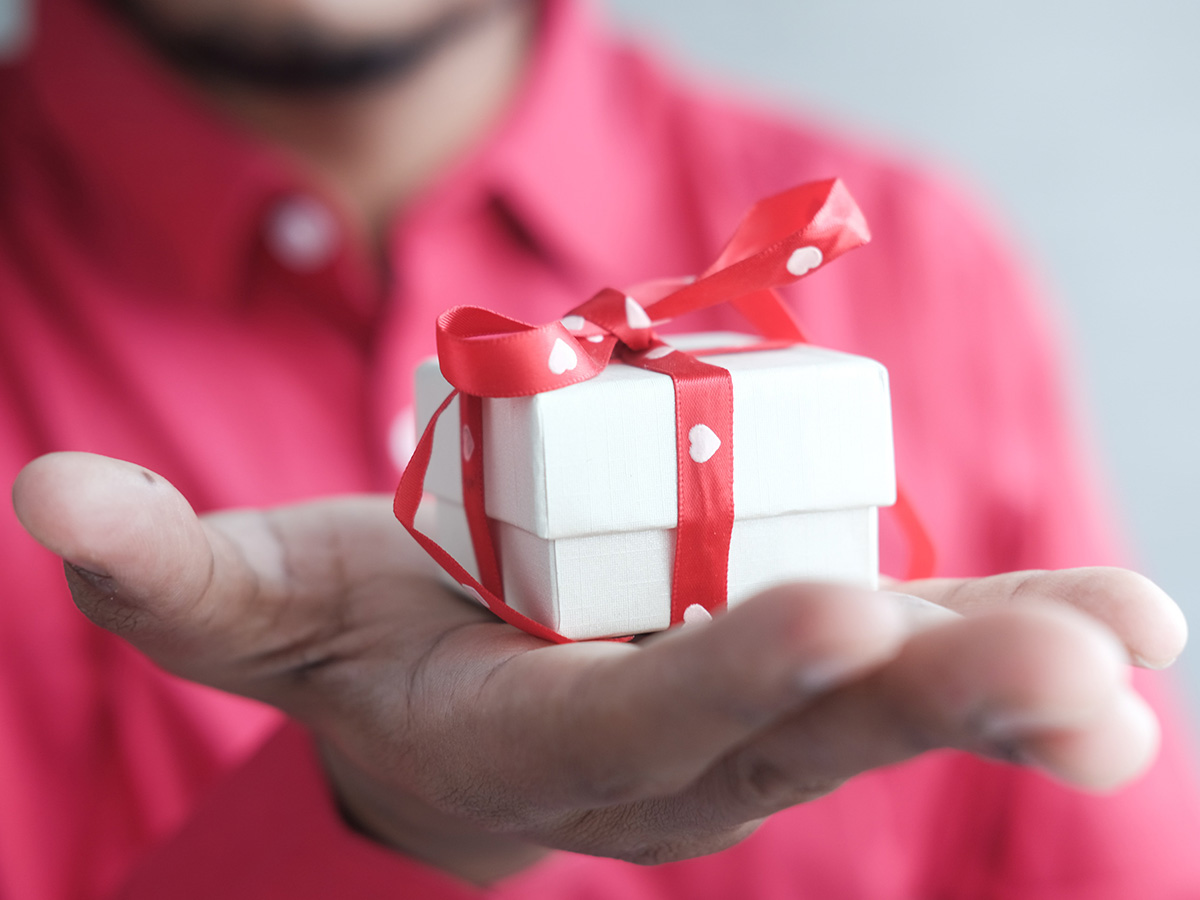A man holding out a giftbox wrapped in a ribbon with hearts