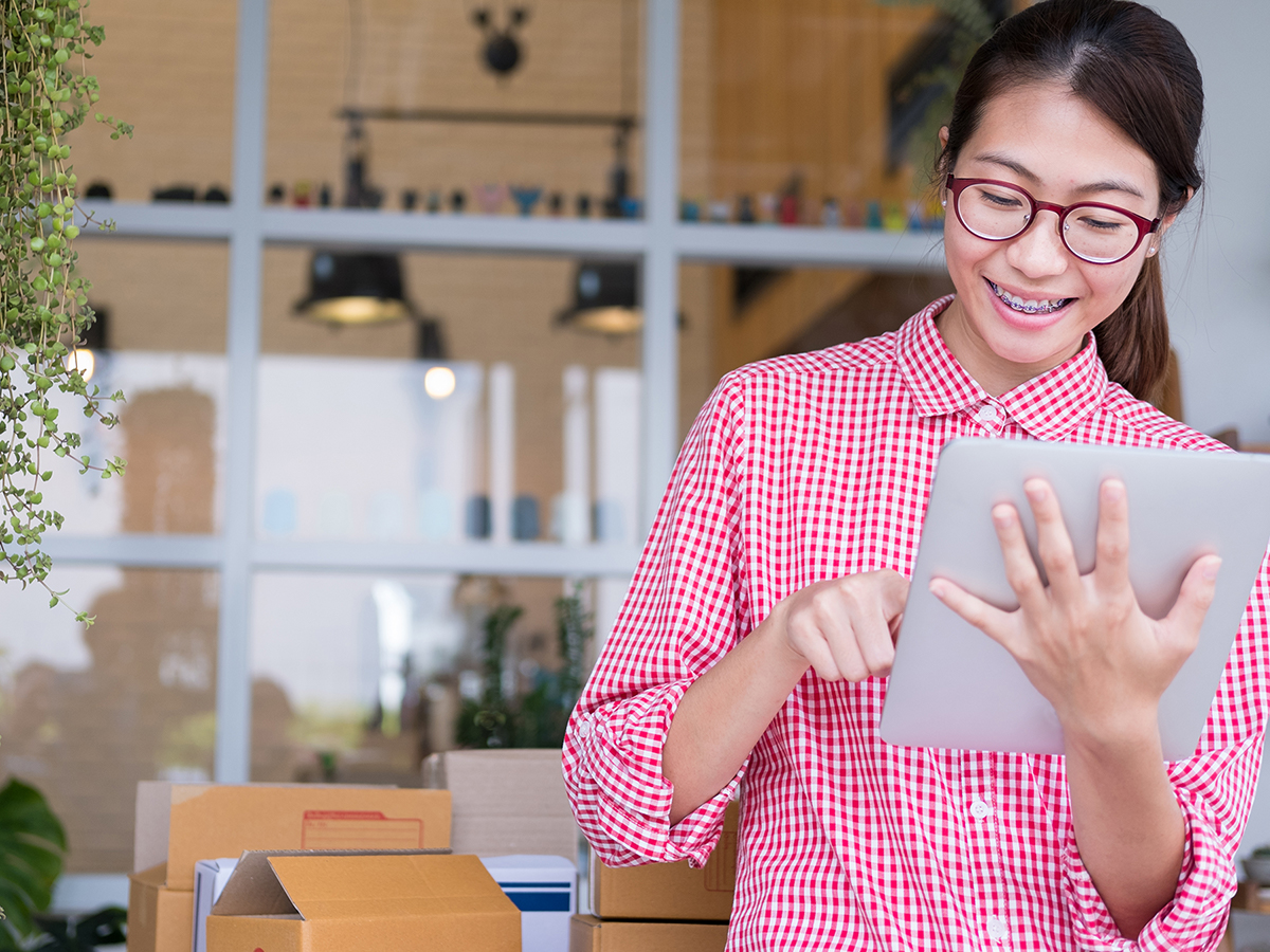 A woman smiling while looking at her laptop with packages behind her